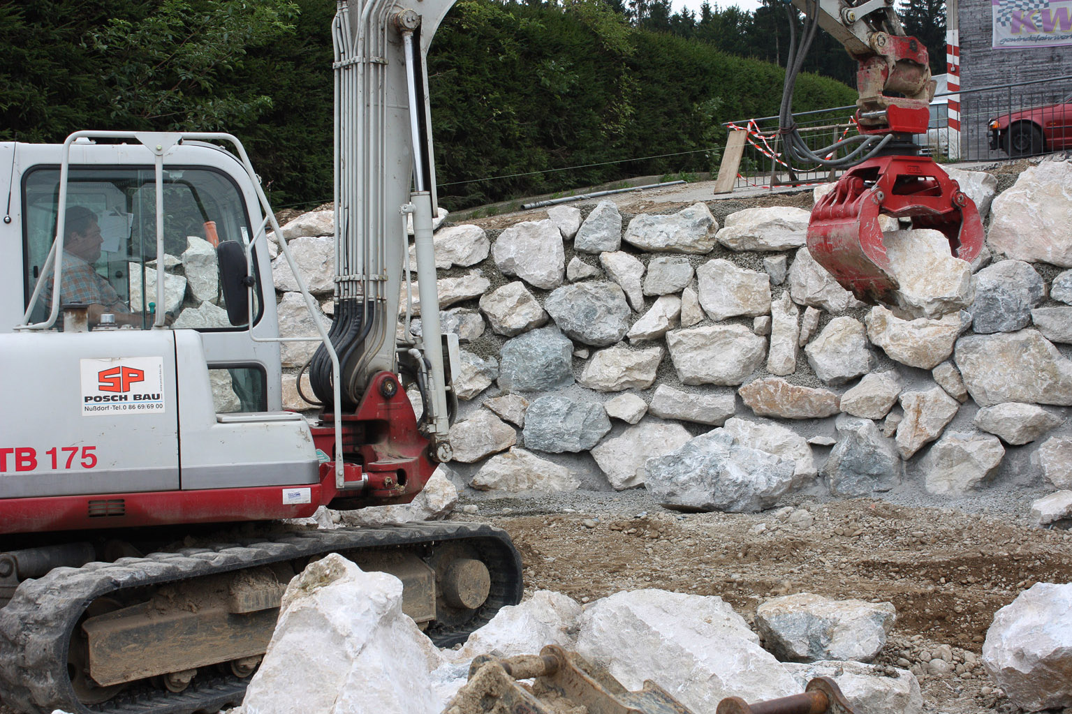 Arbeiten an Naturstein-Mauer mit Minibagger
