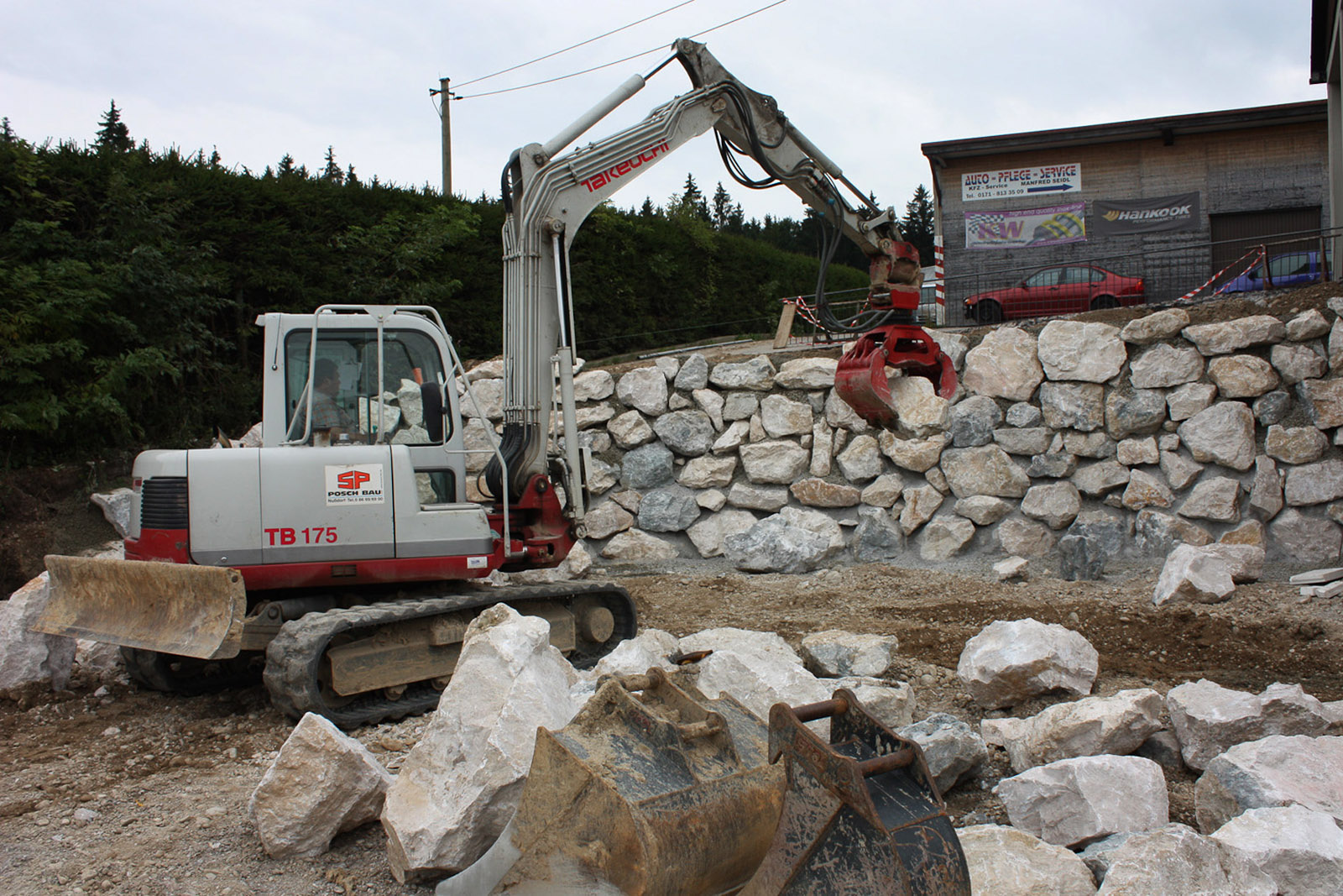 Arbeiten an Naturstein-Mauer mit Minibagger