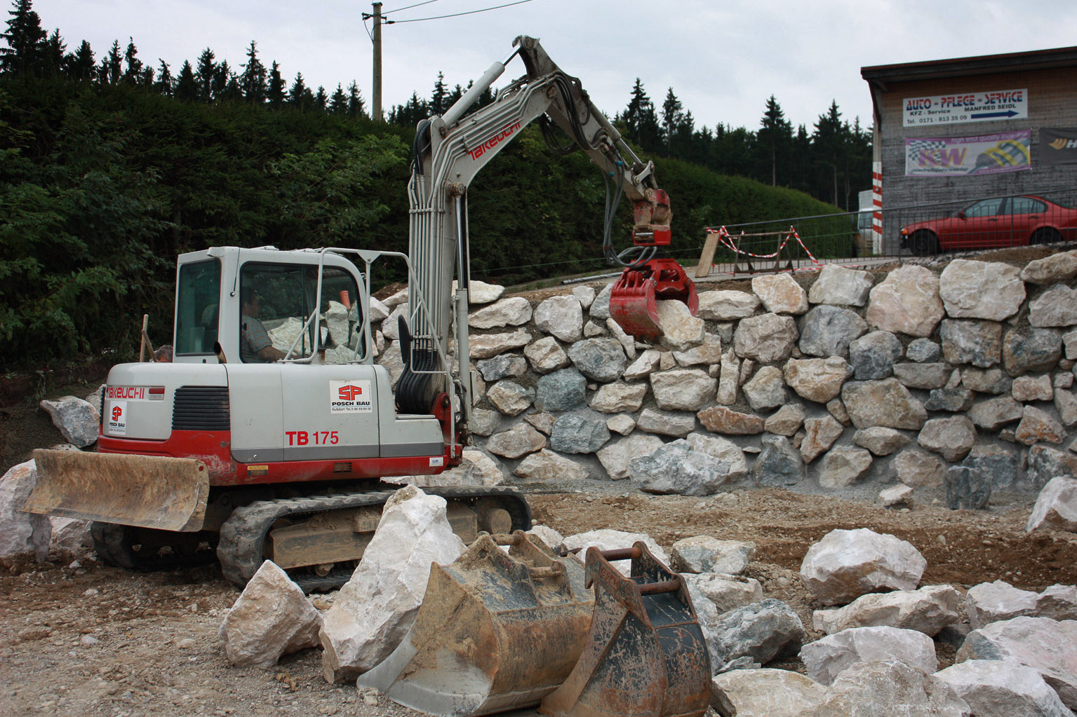 Arbeiten an Naturstein-Mauer mit Minibagger