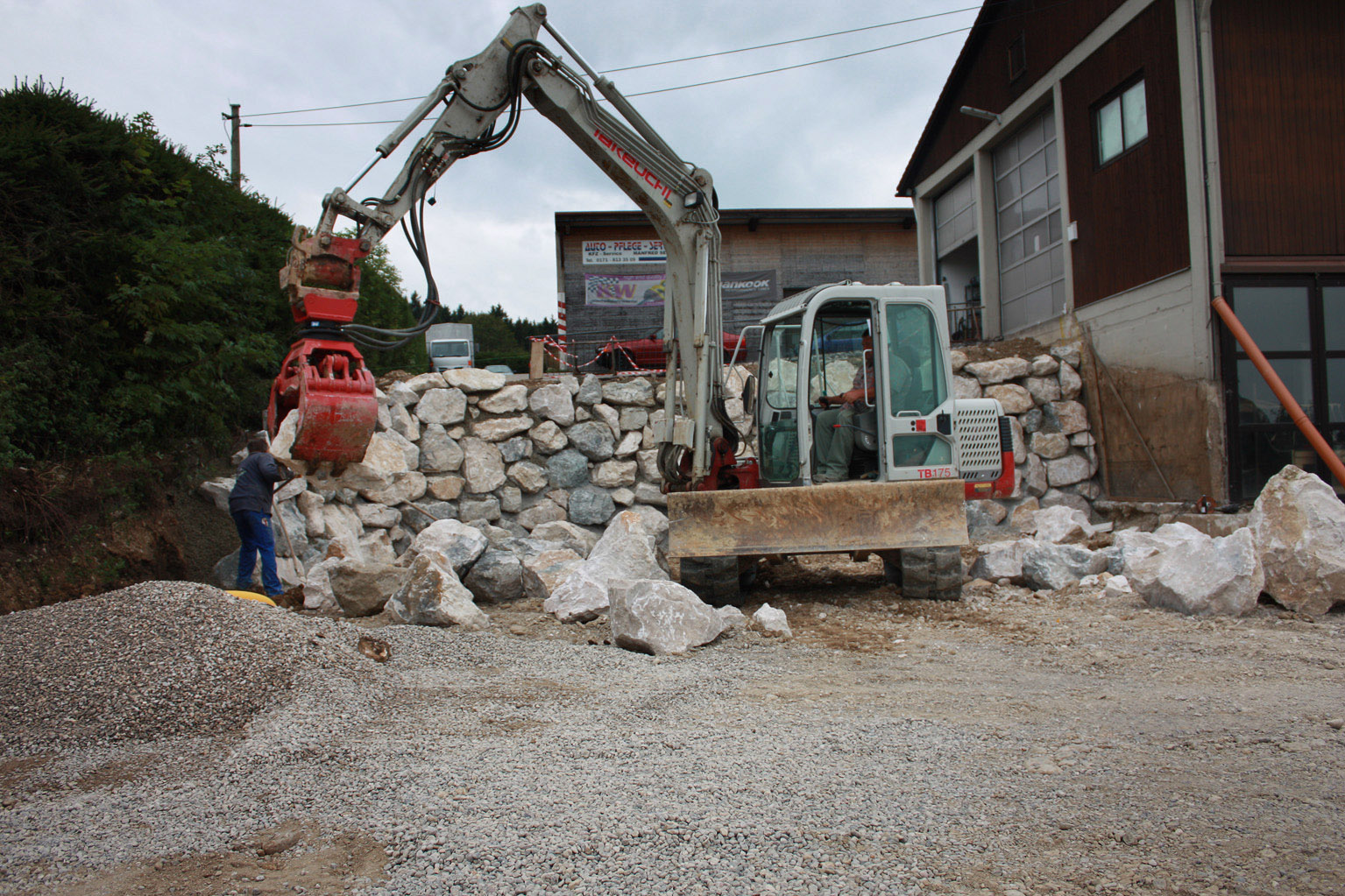 Arbeiten an Naturstein-Mauer mit Minibagger